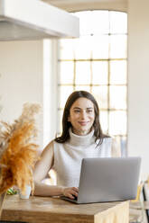 Lächelnde Geschäftsfrau mit Laptop bei der Arbeit zu Hause - DMOF00200
