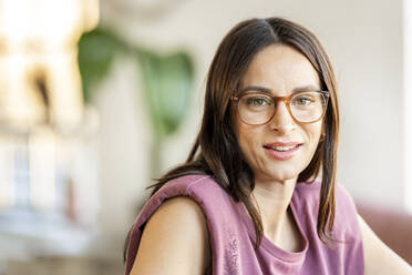 Smiling woman with brown hair wearing eyeglasses at home - DMOF00212