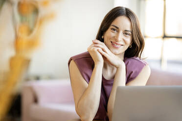 Smiling businesswoman with hand on chin sitting at home - DMOF00213