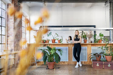 Businesswoman with arms crossed standing by potted plants in living room at home - DMOF00218