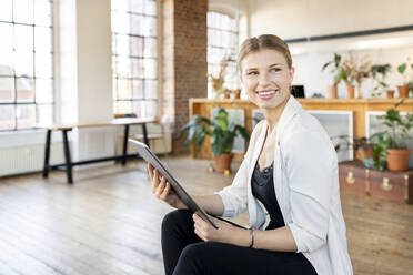 Happy freelancer with tablet PC sitting in living room at home - DMOF00239