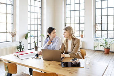 Confident businesswoman in smart casuals sitting by colleague with laptop at home office - DMOF00254