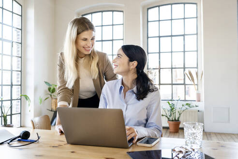 Glückliche Geschäftsfrauen mit Laptop bei der Arbeit im Heimbüro - DMOF00259