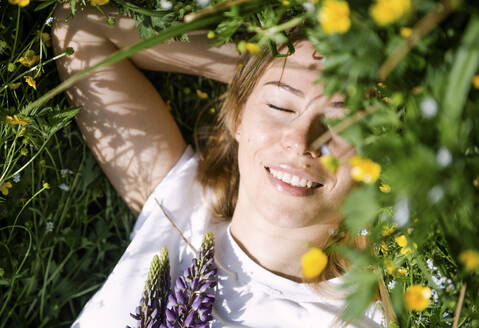 Lächelnde Frau mit geschlossenen Augen im Gras liegend an einem sonnigen Tag - VBUF00058