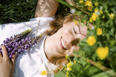 Glückliche Frau mit geschlossenen Augen im Gras liegend an einem sonnigen Tag - VBUF00059