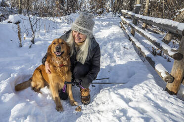 Lächelnde ältere Frau streichelt Hund im Schnee - TETF00583