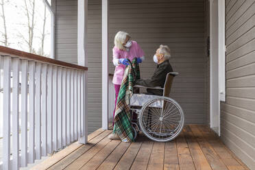 Frau und Mann im Rollstuhl tragen auf der Veranda eine Schutzmaske, um die Übertragung des Coronavirus zu verhindern - TETF00593