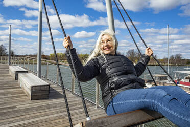 USA, Washington D.C., Senior woman on swing at Wharf District along Potomac River - TETF00599