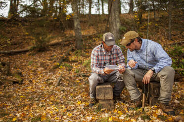Männer mit Angelruten und Kiste auf Baumstämmen sitzend im Herbst - TETF00653