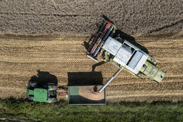 Aerial drone POV combine harvester filling tractor trailer in agricultural field - FSIF05942