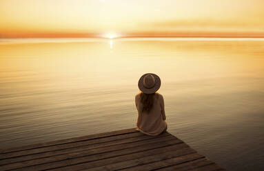 Junge Frau sitzt bei Sonnenuntergang auf einem Steg - TETF00676