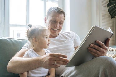 Father reading book to daughter on sofa - TETF00678