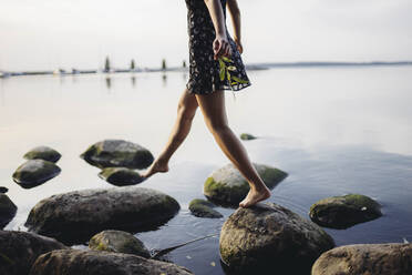 Barefoot woman stepping on rocks in sea - TETF00679