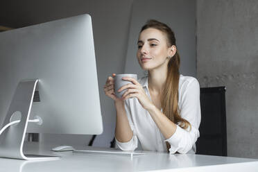 Junge Geschäftsfrau hält Kaffeetasse am Schreibtisch - TETF00683