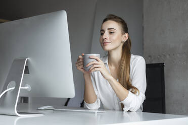 Young businesswoman holding coffee cup at desk - TETF00683