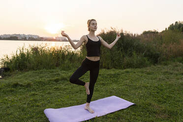 Young woman practicing yoga in park at sunset - TETF00691