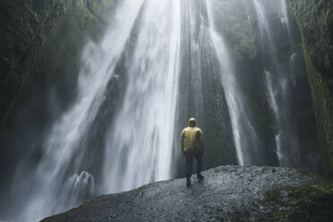 Man wearing yellow raincoat by Seljalandsfoss waterfall in Iceland - TETF00742