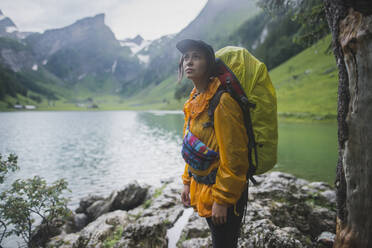 Woman wearing yellow backpack by Seealpsee lake in Appenzell Alps, Switzerland - TETF00745