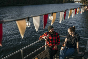 Friends holding beer bottles sitting on boat deck - MJRF00674