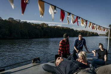 Smiling friends talking with each other sitting on boat deck - MJRF00677