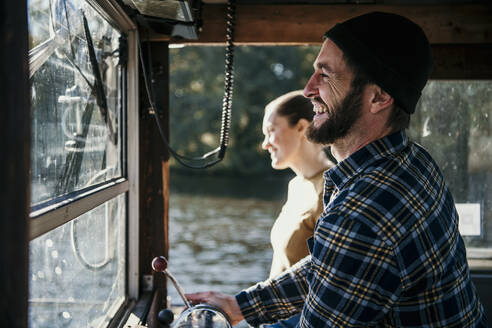 Cheerful man with woman standing in control room of boat - MJRF00690