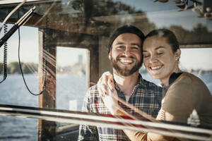 Smiling woman with eyes closed embracing boyfriend standing in control room of boat - MJRF00691