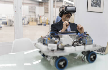 Surprised businessman wearing virtual reality simulator sitting in factory - JCCMF05531