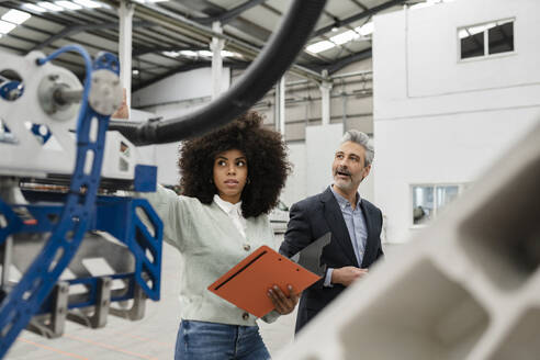 Entwickler erklärt einem Geschäftsmann in einer Fabrik den Roboterarm - JCCMF05536