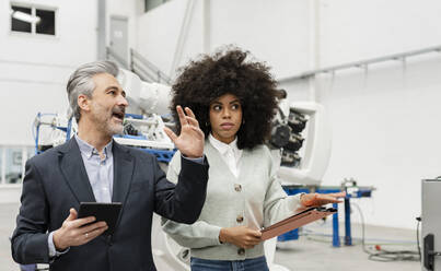 Businessman holding tablet PC discussing with developer in factory - JCCMF05540