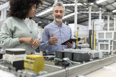 Engineer holding tablet PC explaining to developer about machine in factory - JCCMF05550