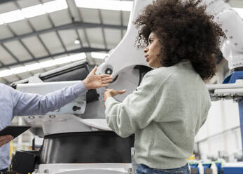 Developer discussing with colleague about robotic arm in factory - JCCMF05557