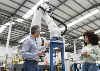 Engineer having discussion about robotic arm in factory - JCCMF05558