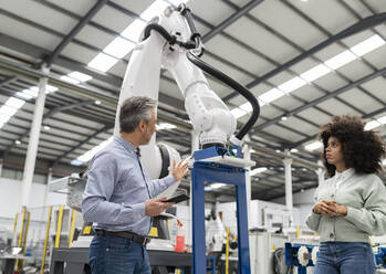 Ingenieur im Gespräch über einen Roboterarm in einer Fabrik - JCCMF05558
