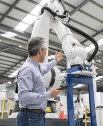 Techniker hält Tablet-PC und zeigt auf Roboterarm in Fabrik - JCCMF05559