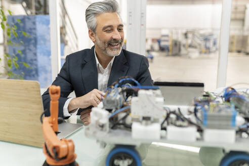 Happy businessman looking at model of robotic vehicle in factory - JCCMF05580