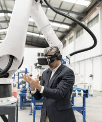 Businessman wearing virtual reality standing with hands cupped in factory - JCCMF05598