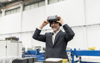 Glücklicher Geschäftsmann, der einen Virtual-Reality-Simulator in einer Fabrik entfernt - JCCMF05600