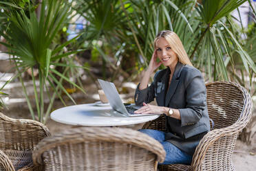 Lächelnde schöne Geschäftsfrau mit Laptop in einem Straßencafé sitzend - DLTSF02776