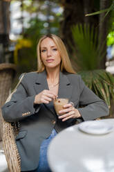 Blonde Geschäftsfrau mit Kaffeetasse in einem Straßencafé - DLTSF02782