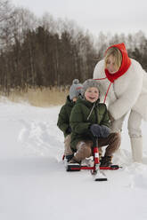 Glückliche Mutter, die ihre Söhne auf dem Schlitten sitzend im Winter schiebt - SEAF00675