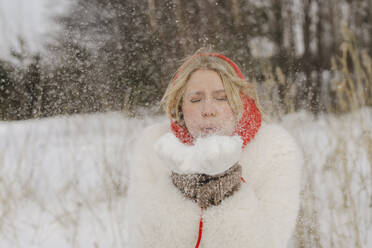 Blond woman with eyes closed blowing snow - SEAF00676