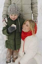 Junge mit Keks in der Hand steht mit Eltern im Schnee - SEAF00679