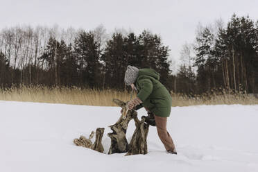 Junge spielt mit Baumstamm auf Schnee im Winter - SEAF00691
