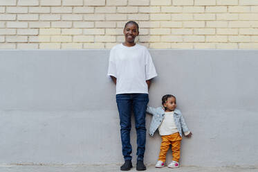 Smiling woman with daughter standing in front of wall - PGF01021