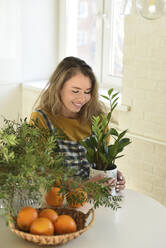 Lächelnde Frau mit Zimmerpflanze am Tisch in der Küche sitzend - VBUF00063