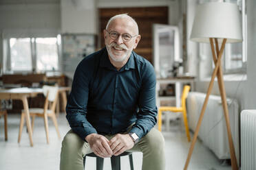 Happy senior businessman sitting on stool in office - JOSEF07329