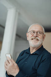 Lächelnder älterer Mann mit Mobiltelefon im Büro - JOSEF07336
