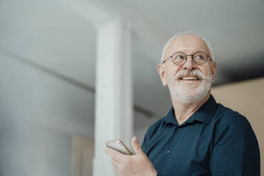 Glücklicher älterer Mann mit Smartphone im Büro - JOSEF07337