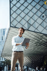 Hübscher Geschäftsmann mit Tablet-PC vor einem modernen Gebäude stehend - GUSF07135