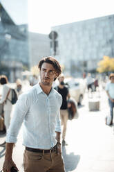 Handsome businessman with hand in pocket in city on sunny day - GUSF07154